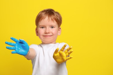 Photo of Little boy with hands painted in Ukrainian flag colors on yellow background, space for text. Love Ukraine concept