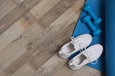 Photo of Dumbbells, sneakers and mat on wooden floor, above view. Space for text