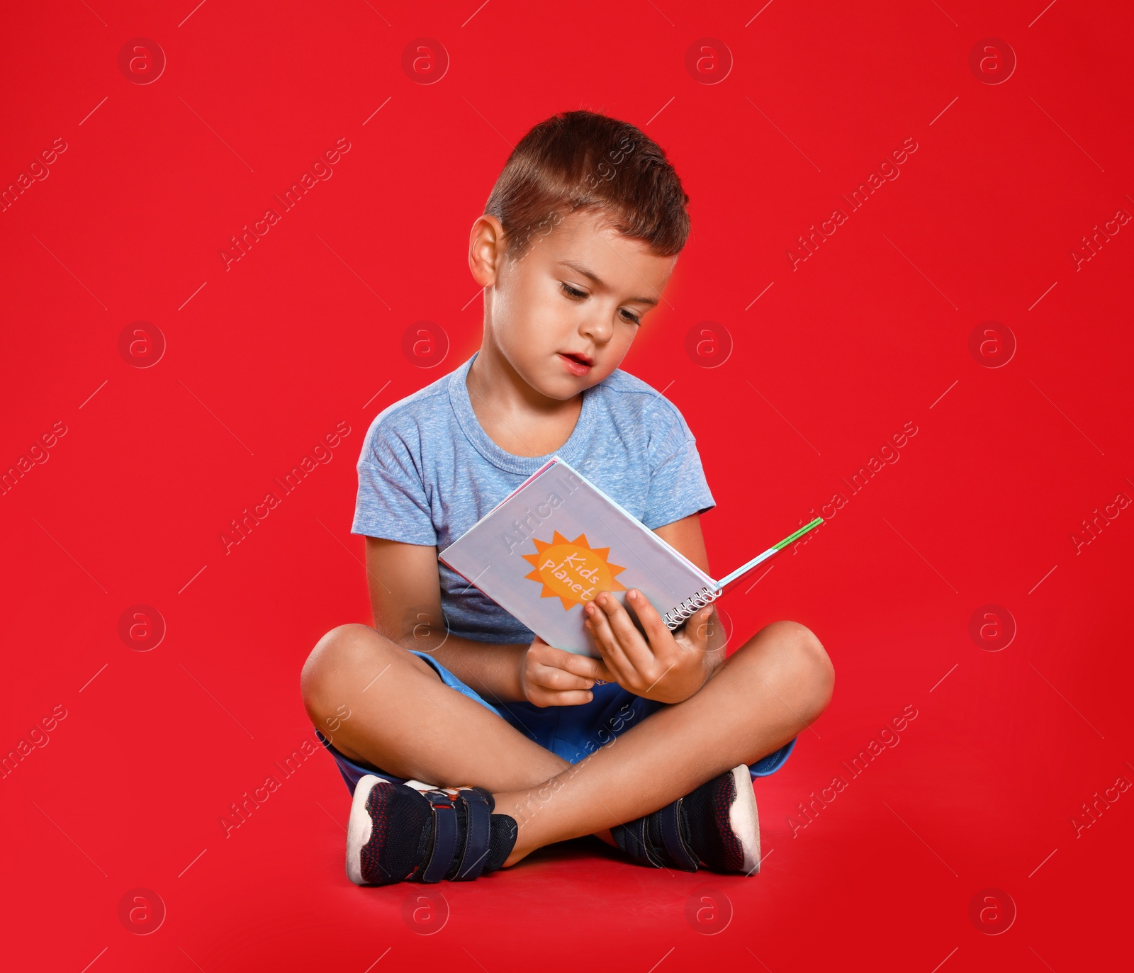 Photo of Cute little boy reading book on red background