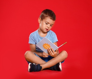 Cute little boy reading book on red background