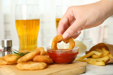 Woman dipping crunchy fried onion ring in tomato sauce, closeup