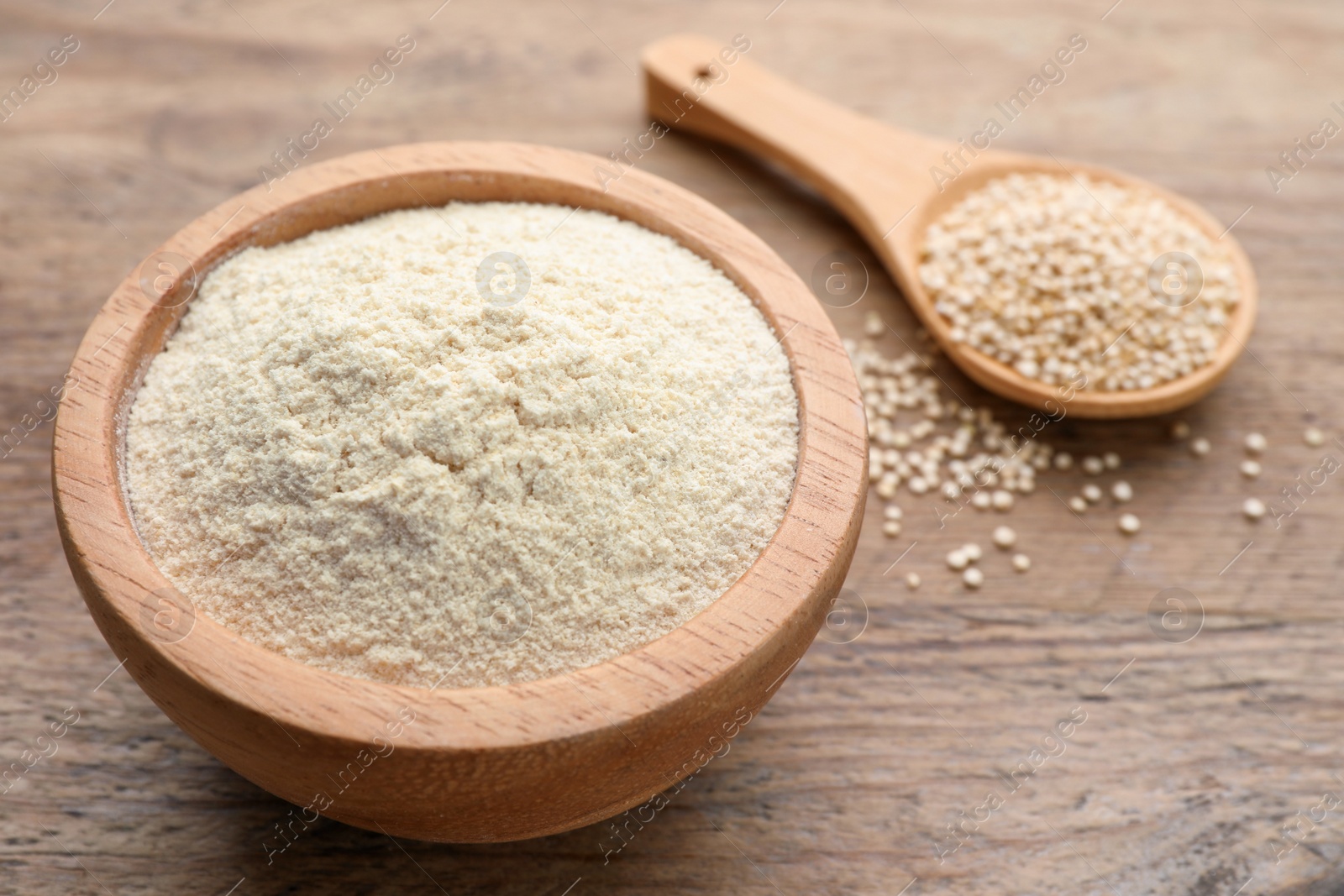 Photo of Quinoa flour in bowl and spoon with seeds on wooden table