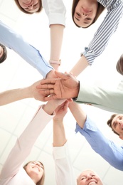 Photo of People putting hands together on light background, bottom view. Unity concept