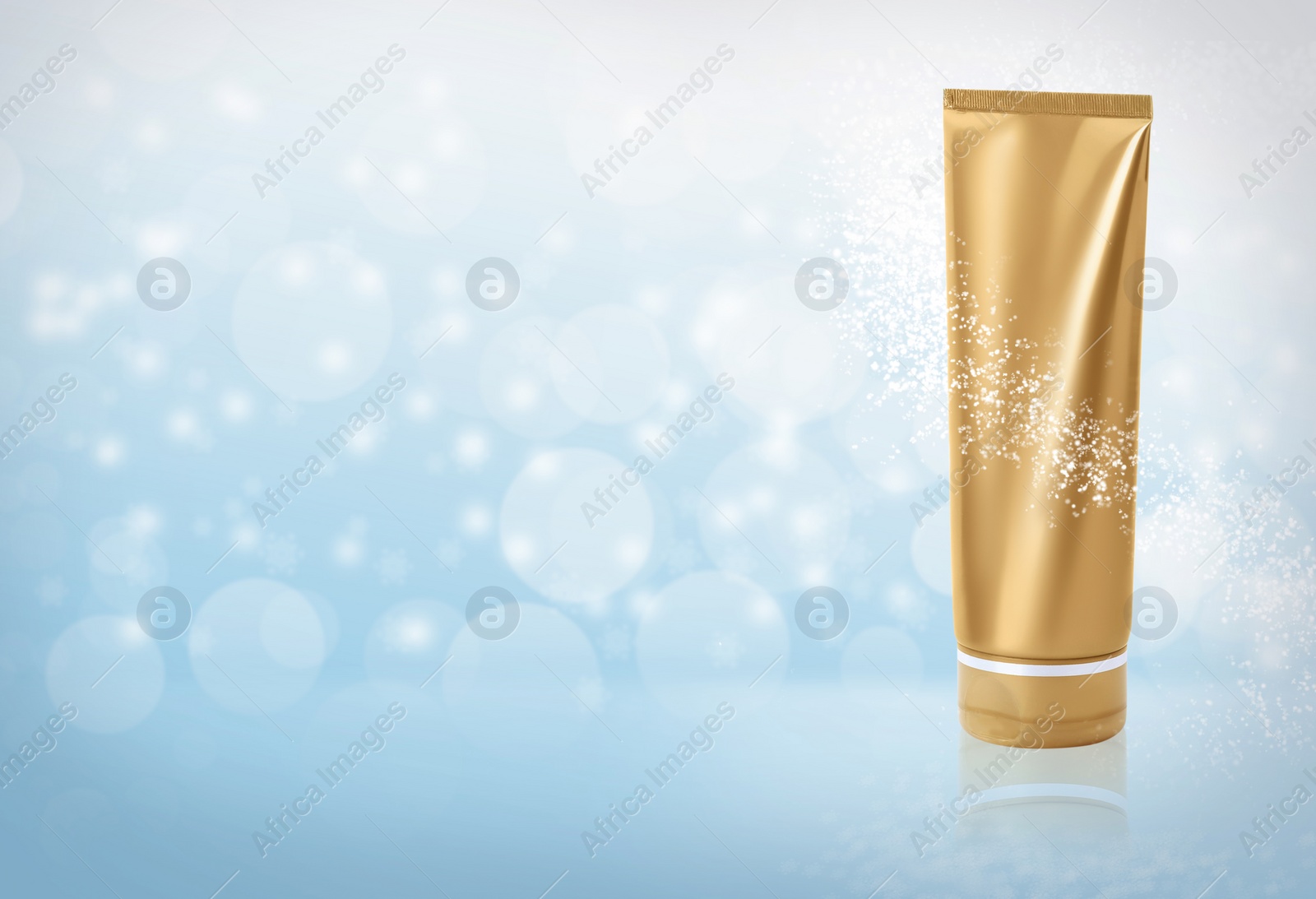 Image of Tube of cosmetic product on light blue background with blurred snowflakes, space for text. Winter skin care