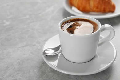 Cup of fresh coffee and croissant on grey table. Space for text