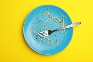 Photo of Dirty plate with food leftovers and fork on yellow background, top view