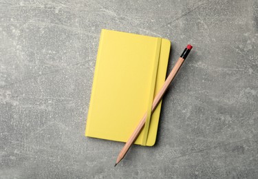 Yellow planner and pencil on grey table, top view
