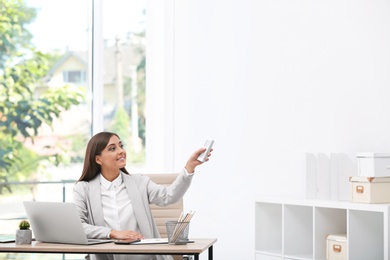 Photo of Young woman with air conditioner remote in office