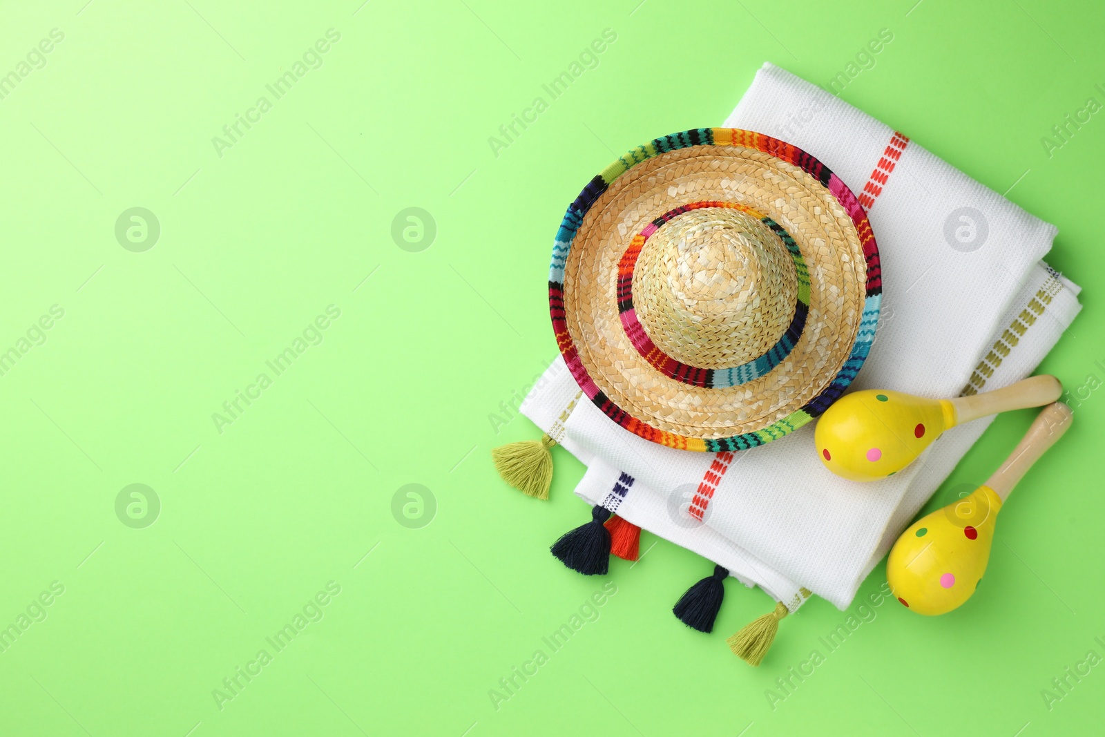 Photo of Mexican sombrero hat, maracas and poncho on green background, flat lay. Space for text