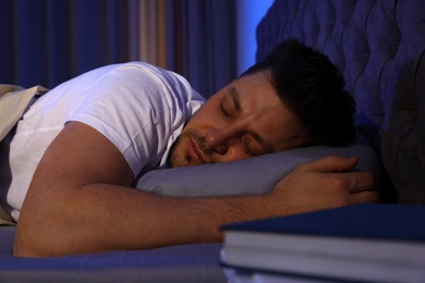 Photo of Handsome man sleeping on pillow in dark room at night. Bedtime