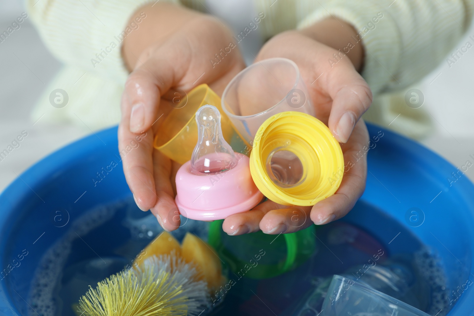 Photo of Woman holding baby bottle nipples above basin with water, closeup. Washing dishes