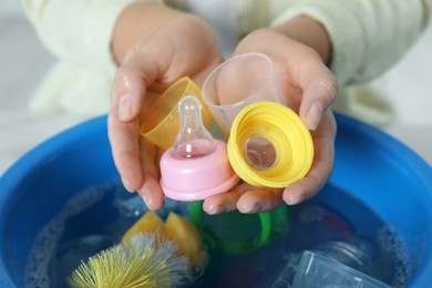 Photo of Woman holding baby bottle nipples above basin with water, closeup. Washing dishes