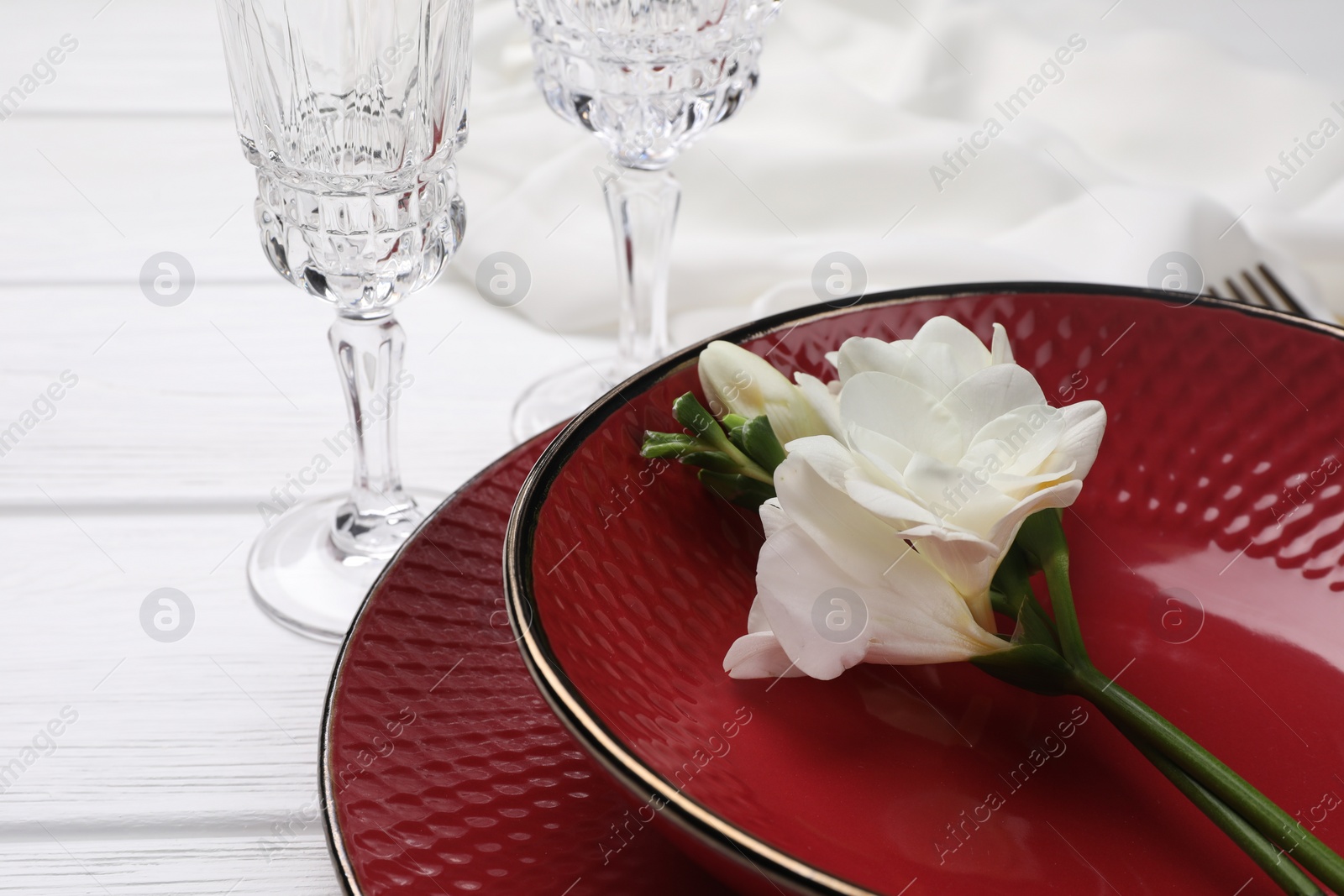 Photo of Dishes with flower and glasses on white wooden table, closeup