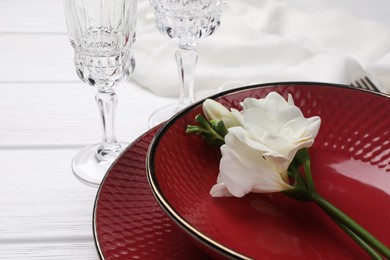 Photo of Dishes with flower and glasses on white wooden table, closeup