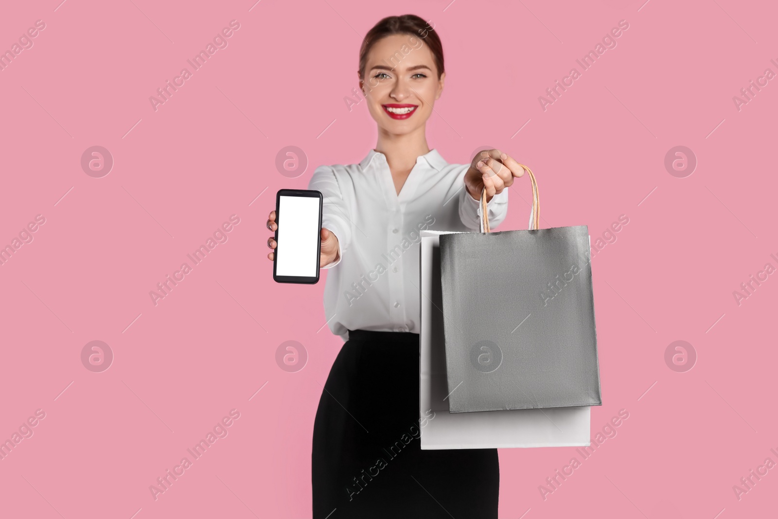 Photo of Happy young woman holding shopping bags and smartphone against light pink background, focus on hands. Big sale