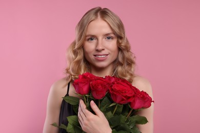 Photo of Beautiful woman with blonde hair holding bouquet of red roses on pink background