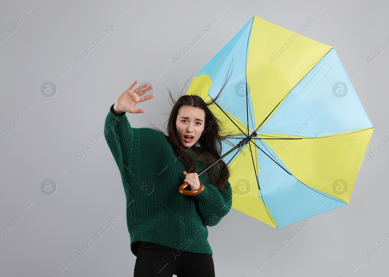 Photo of Emotional woman with umbrella caught in gust of wind on grey background