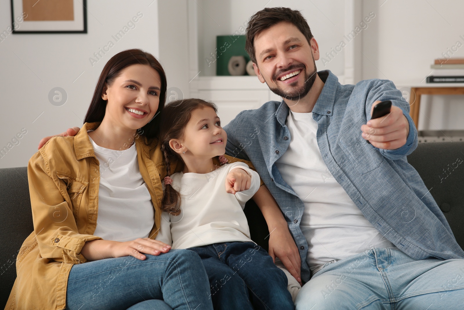 Photo of Happy family watching movie at home. Father changing TV channels with remote control