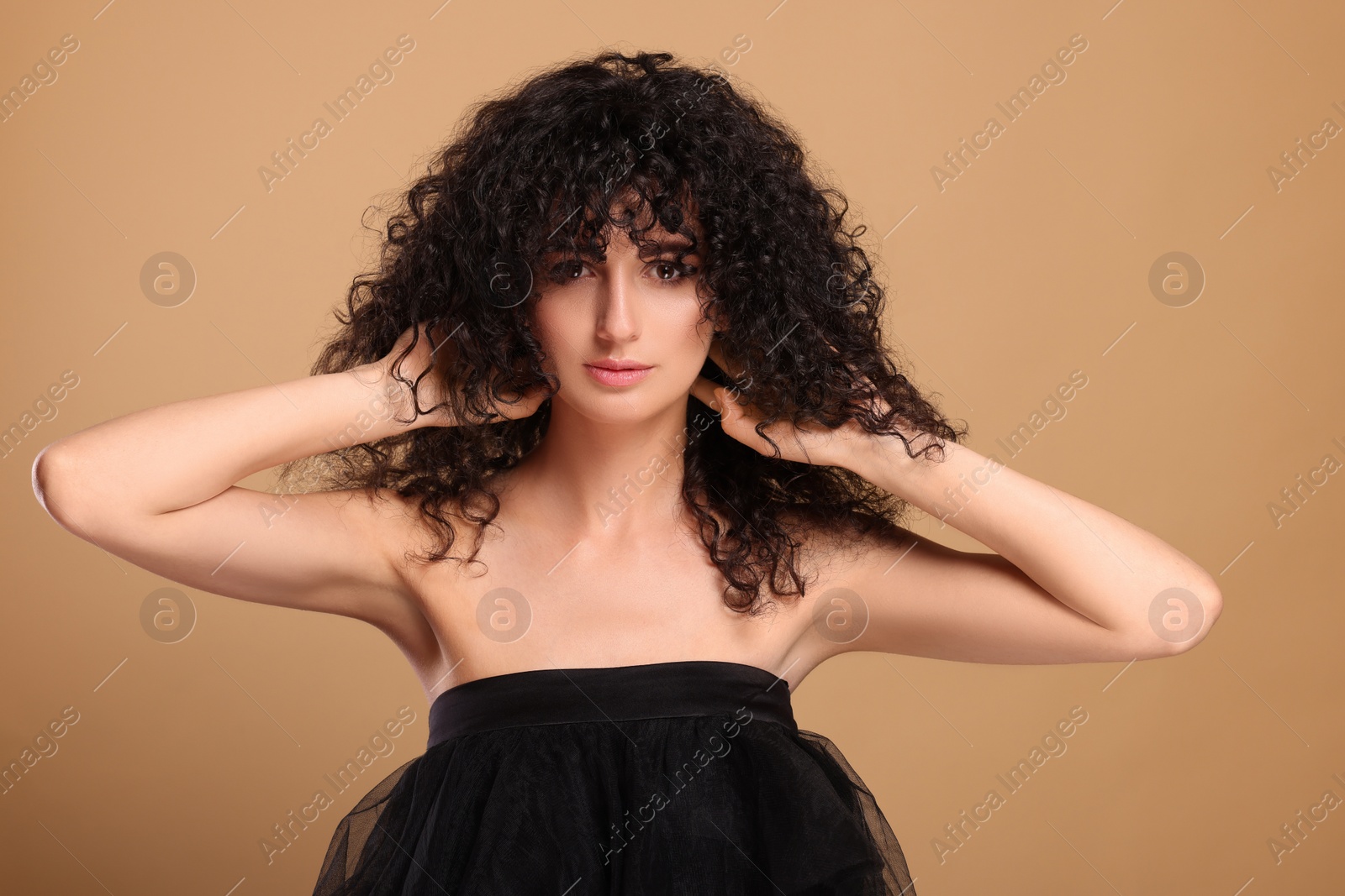 Photo of Beautiful young woman with long curly hair on beige background