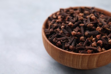 Photo of Aromatic cloves in bowl on gray table, closeup. Space for text