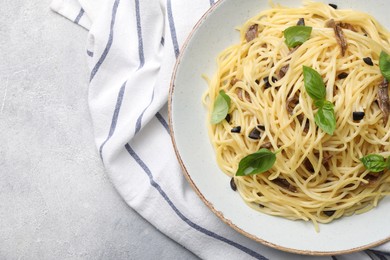 Photo of Delicious pasta with anchovies, olives and basil on light grey table, top view. Space for text