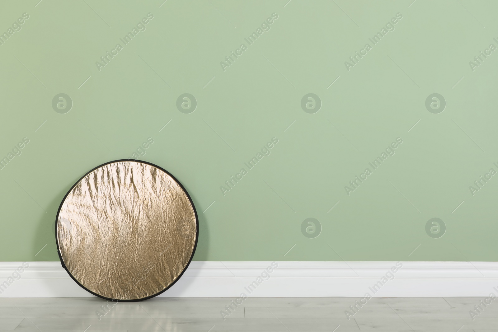 Photo of Studio reflector near pale green wall in room, space for text. Professional photographer's equipment