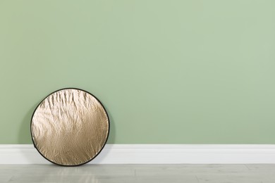 Studio reflector near pale green wall in room, space for text. Professional photographer's equipment