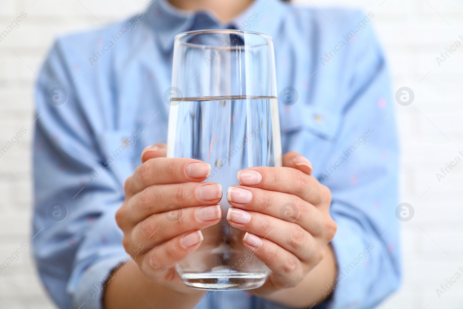 Photo of Woman holding glass of water near brick wall, closeup. Refreshing drink
