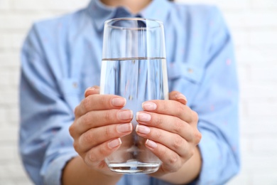 Woman holding glass of water near brick wall, closeup. Refreshing drink