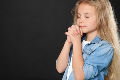 Photo of Girl with clasped hands praying on black background, space for text