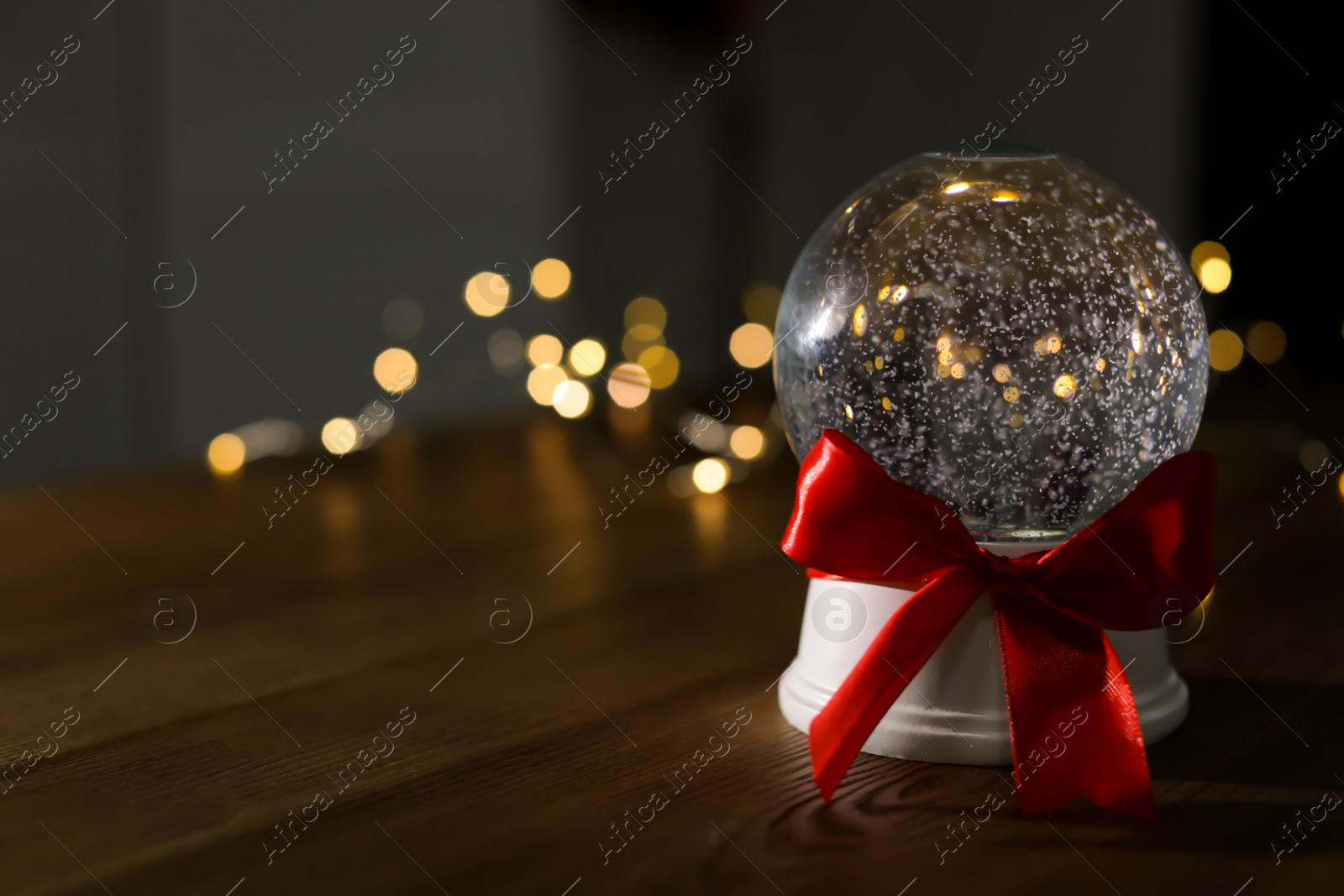 Photo of Christmas snow globe with red bow on wooden table. Space for text