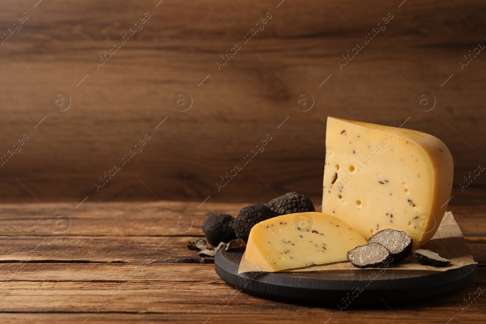 Photo of Board with delicious cheese and fresh black truffles on wooden table. Space for text