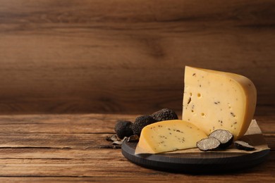 Board with delicious cheese and fresh black truffles on wooden table. Space for text