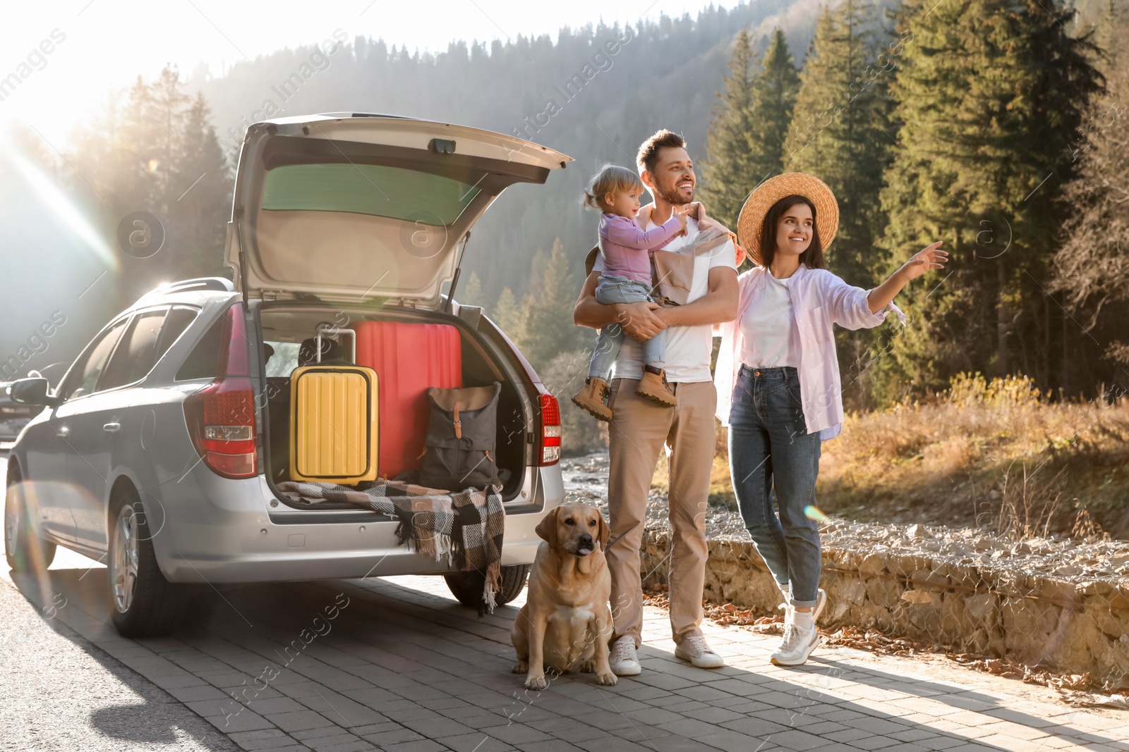 Photo of Parents, their daughter and dog near car outdoors. Family traveling with pet