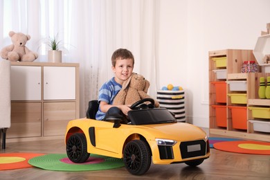 Photo of Little child with bunny driving toy car in room