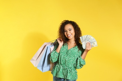 Young African-American woman with money and shopping bags on color background