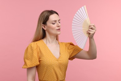 Photo of Beautiful woman waving yellow hand fan to cool herself on pink background