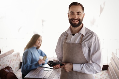 Photo of Waiter holding payment terminal near table with client at restaurant