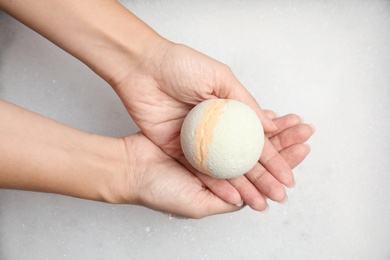 Photo of Woman holding bath bomb over foam, top view