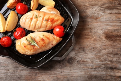 Grill pan with fried chicken breast and garnish on wooden background, top view. Space for text