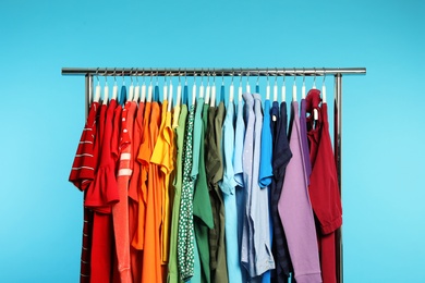 Wardrobe rack with different bright clothes on color background