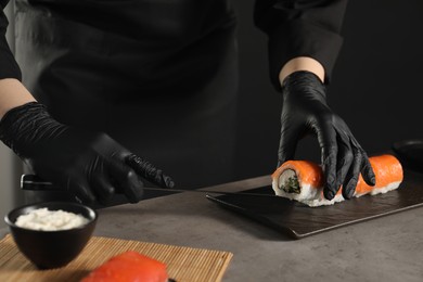 Chef in gloves making sushi rolls at grey table, closeup