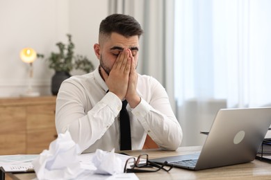 Photo of Overwhelmed man sitting at table with laptop and documents in office