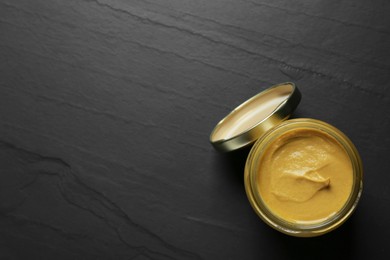 Spicy mustard in glass jar on black table, top view. Space for text