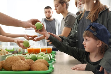 Volunteer giving apple to poor girl indoors