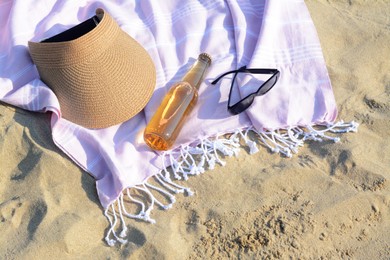 Photo of Pink blanket with stylish visor cap, sunglasses and bottle of beer on sandy beach, above view