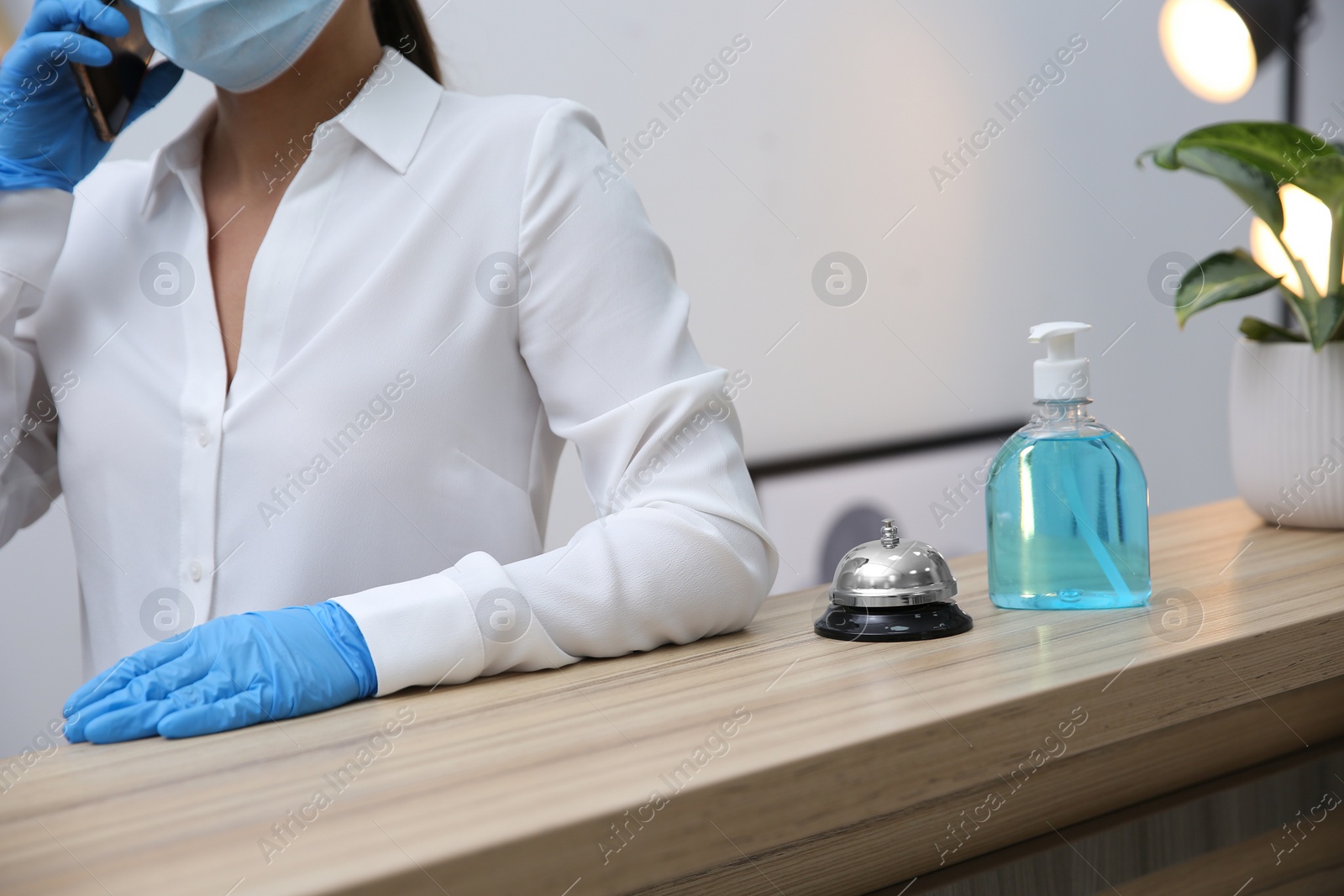 Photo of Receptionist at countertop in hotel, focus on dispenser bottle with antiseptic gel and service bell