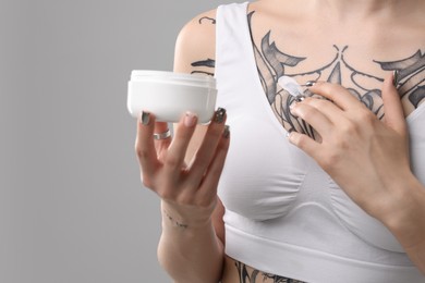 Woman applying healing cream onto her tattoos against grey background, closeup. Space for text