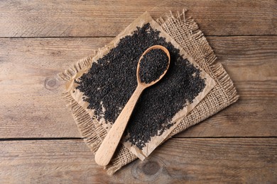 Photo of Black sesame seeds and spoon on wooden table, flat lay