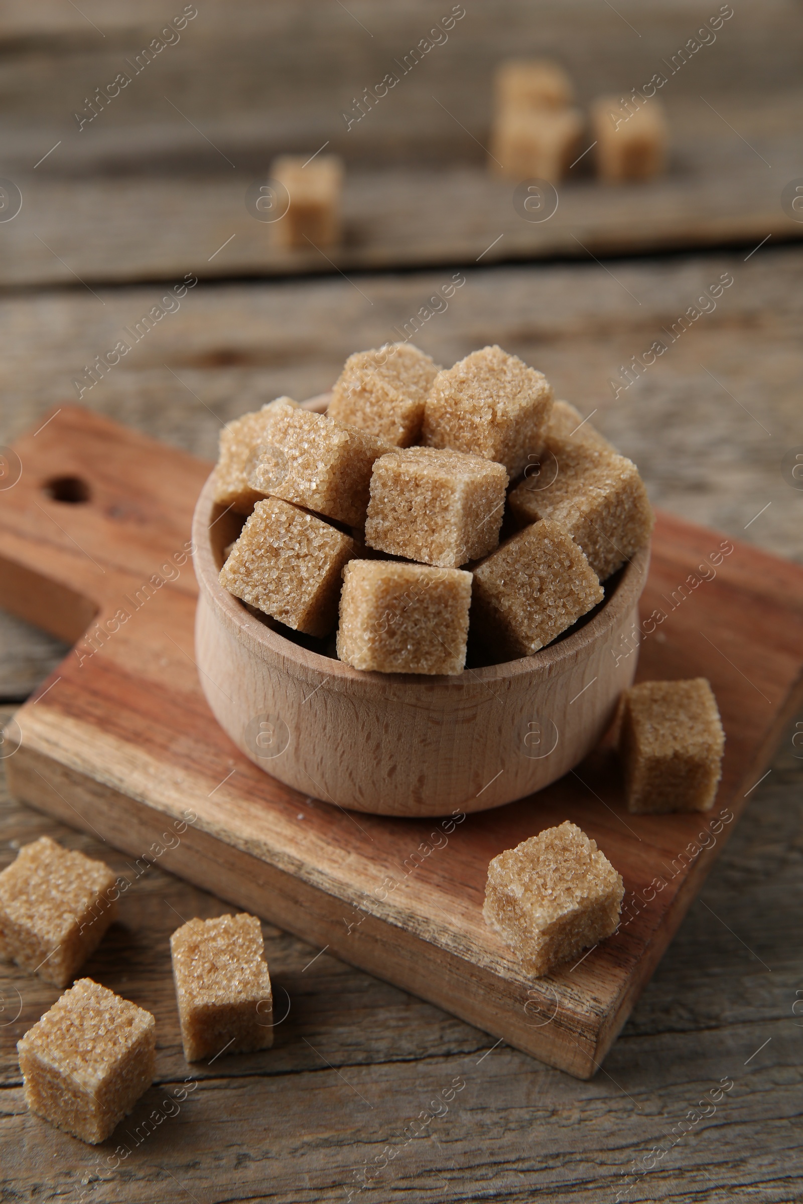 Photo of Brown sugar cubes in bowl on wooden table, closeup